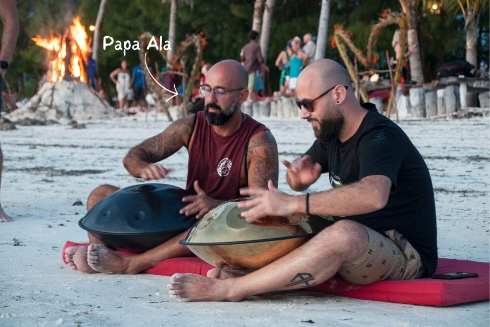 Ala, founder of TribeX, playing handpan on the beach at sunset
