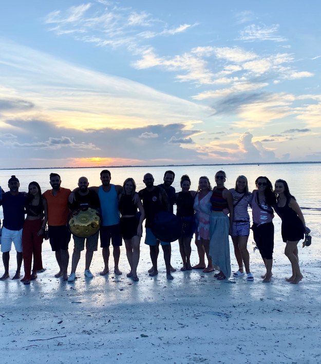 The whole TribeX group standing in a line on the beach as the sun goes down